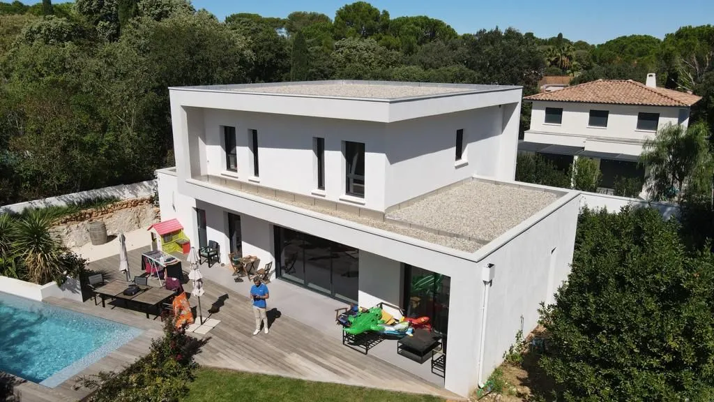 Vue aérienne de la villa : deux volumes blancs à toiture-terrasse, terrasse en bois et piscine